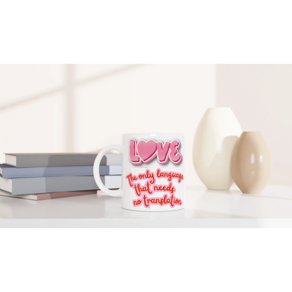 White ceramic mug on a counter with colorful text printed on it saying: LOVE, the only language that needs no translation. Front vue
